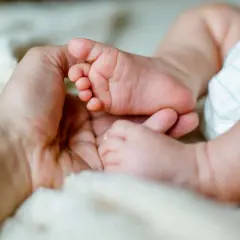 Dłoń dorosłego obejmuje stópkę niemowlęcia na miękkim tle.