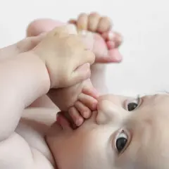 Dziecko wkłada stópkę do buzi, patrząc w górę.