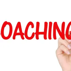 Ręka pisze czerwonym markerem słowo "COACHING" na białym tle.