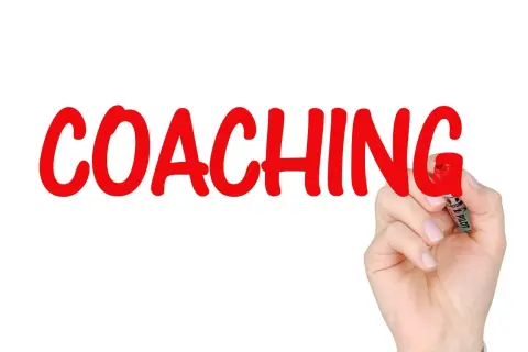 Ręka pisze czerwonym markerem słowo "COACHING" na białym tle.